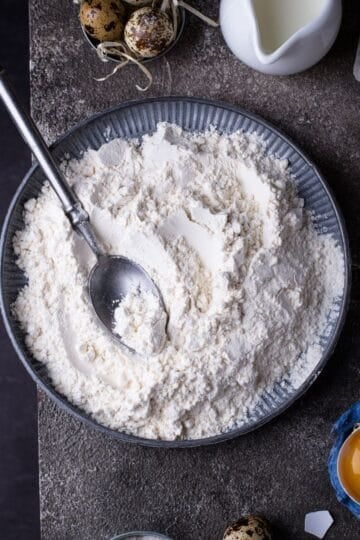 A bowl of flour on a dark background with a spoon.