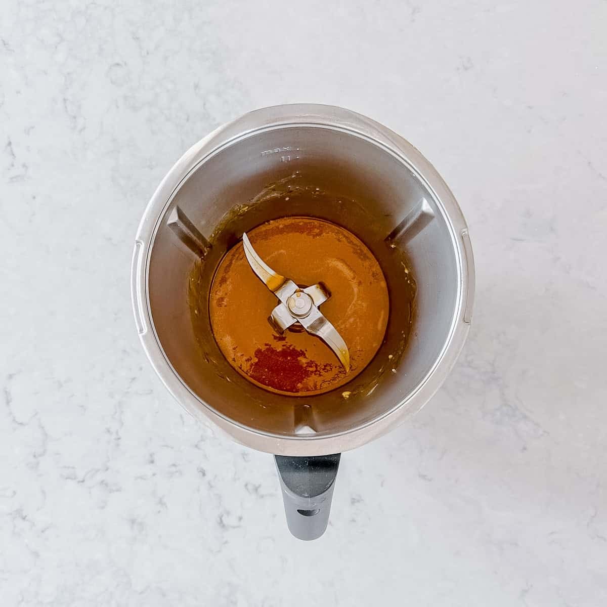 Overhead view of a Thermomix bowl containing melted butter set on a light marble worktop.