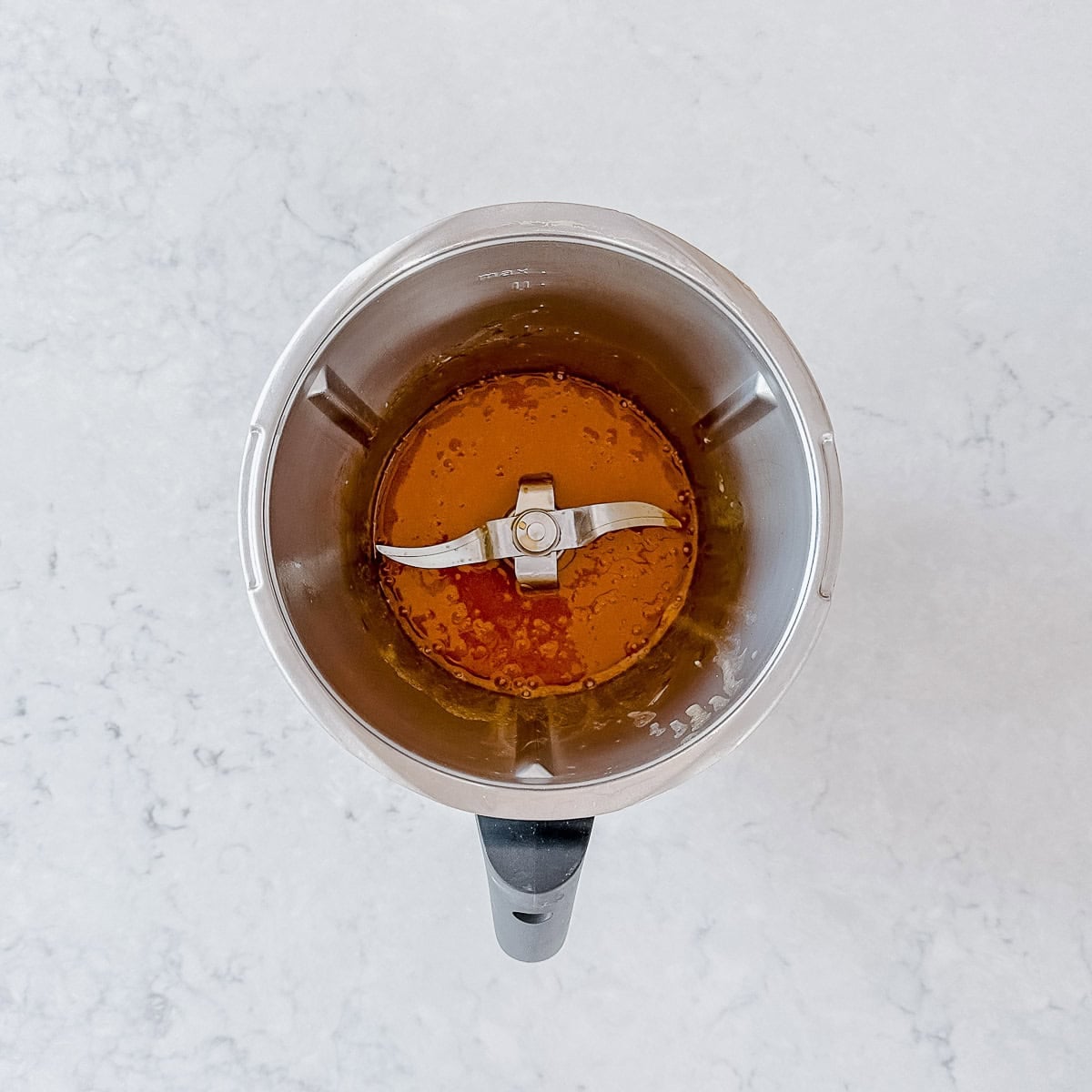 Overhead view of a Thermomix jug containing butter, set on a light marble worktop.