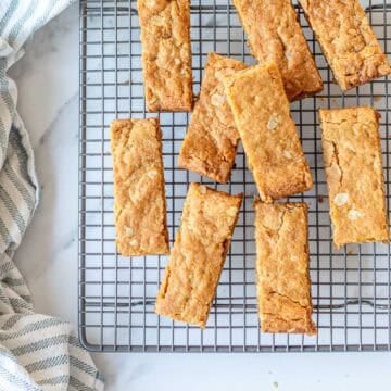 Golden homemade Anzac Slice cut into bars and arranged on a cooling rack with a striped tea towel.
