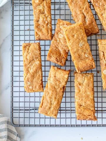 Golden homemade Anzac Slice cut into bars and arranged on a cooling rack with a striped tea towel.
