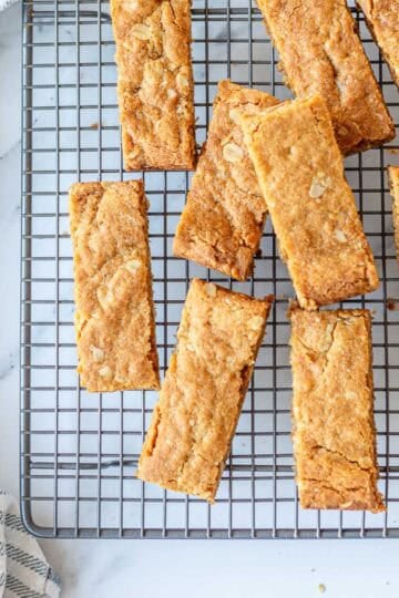 Golden homemade Anzac Slice cut into bars and arranged on a cooling rack with a striped tea towel.