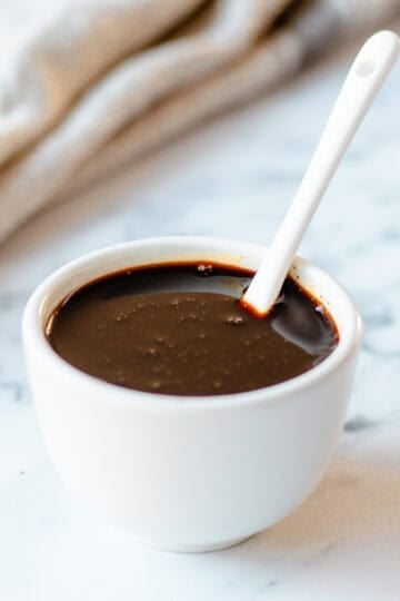 A white bowl filled with balsamic glaze, with a white spoon.