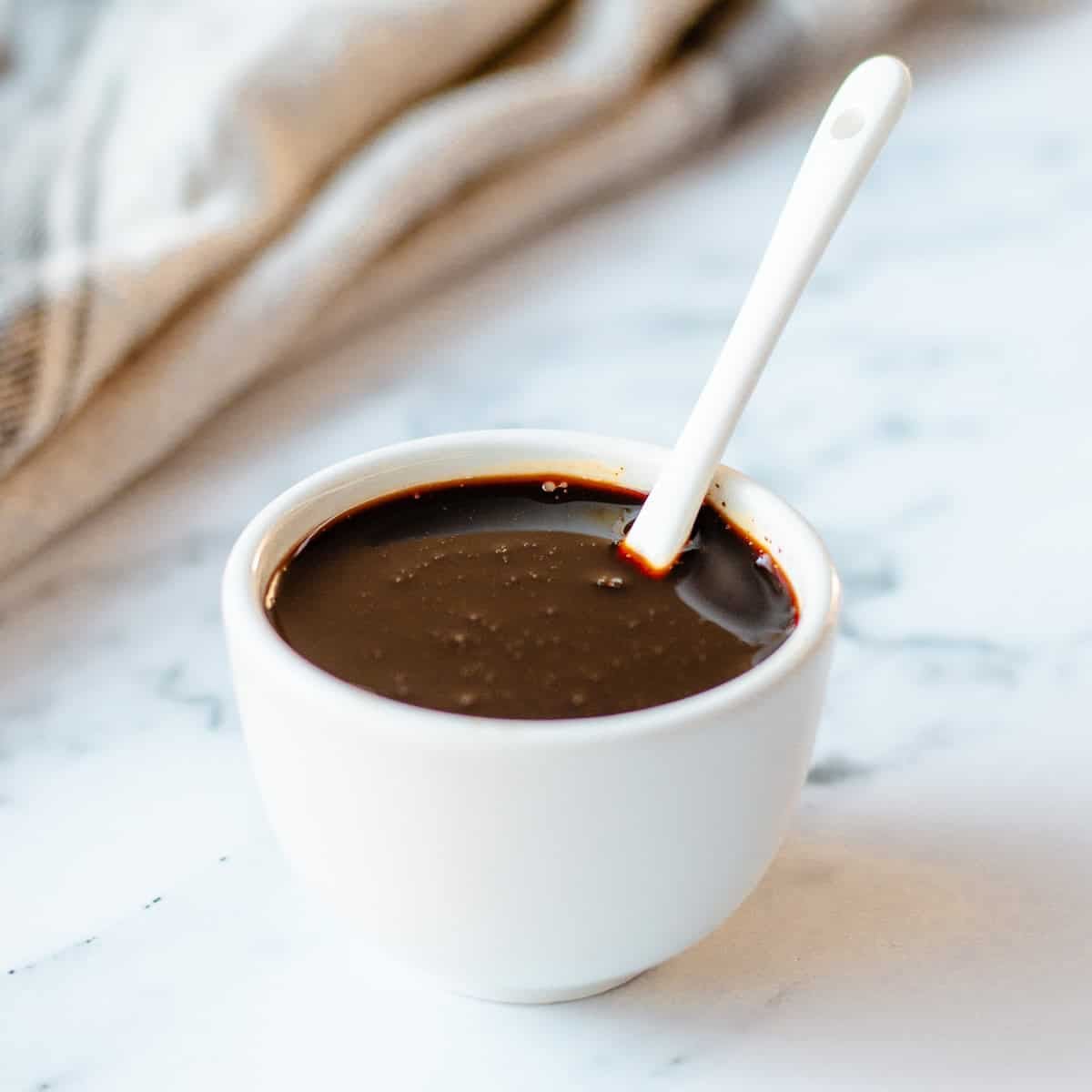 A white bowl filled with balsamic glaze, with a white spoon.
