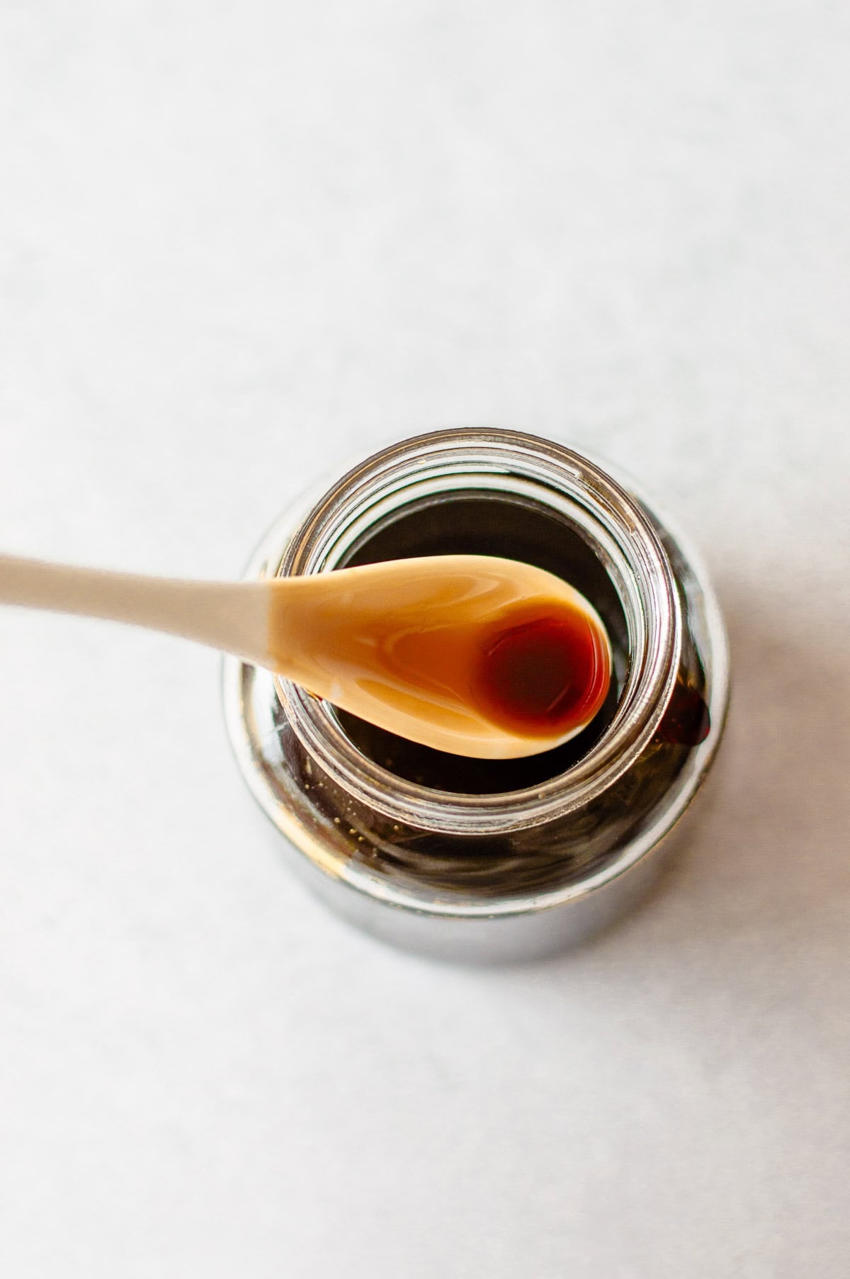 A spoonful of teriyaki sauce held over an open glass jar.