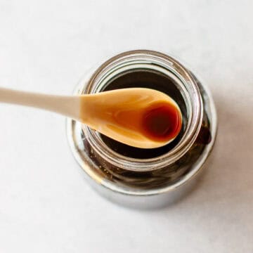A spoonful of teriyaki sauce held over an open glass jar.