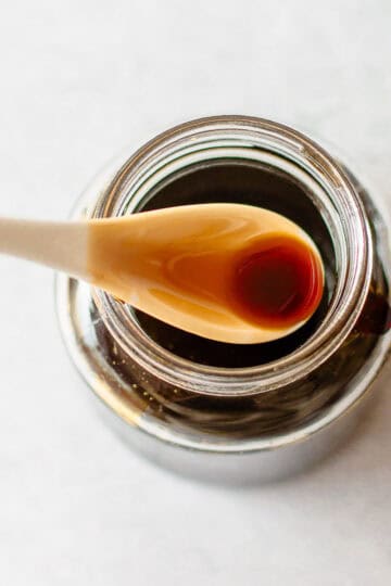 A spoonful of teriyaki sauce held over an open glass jar.