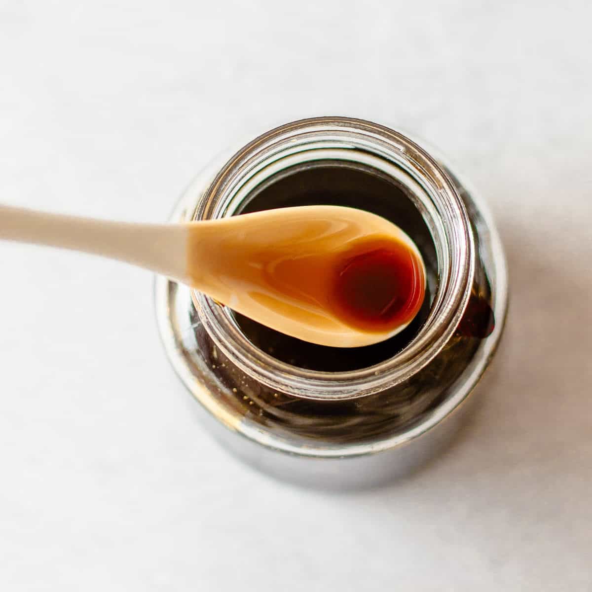 A spoonful of teriyaki sauce held over an open glass jar.