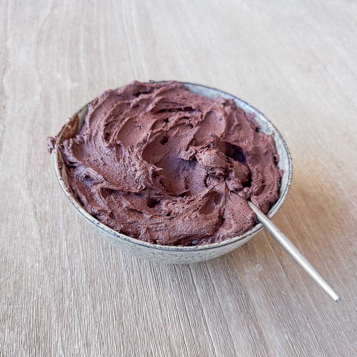 Finished chocolate buttercream swirled in a speckled grey bowl with a spoon resting in it.
