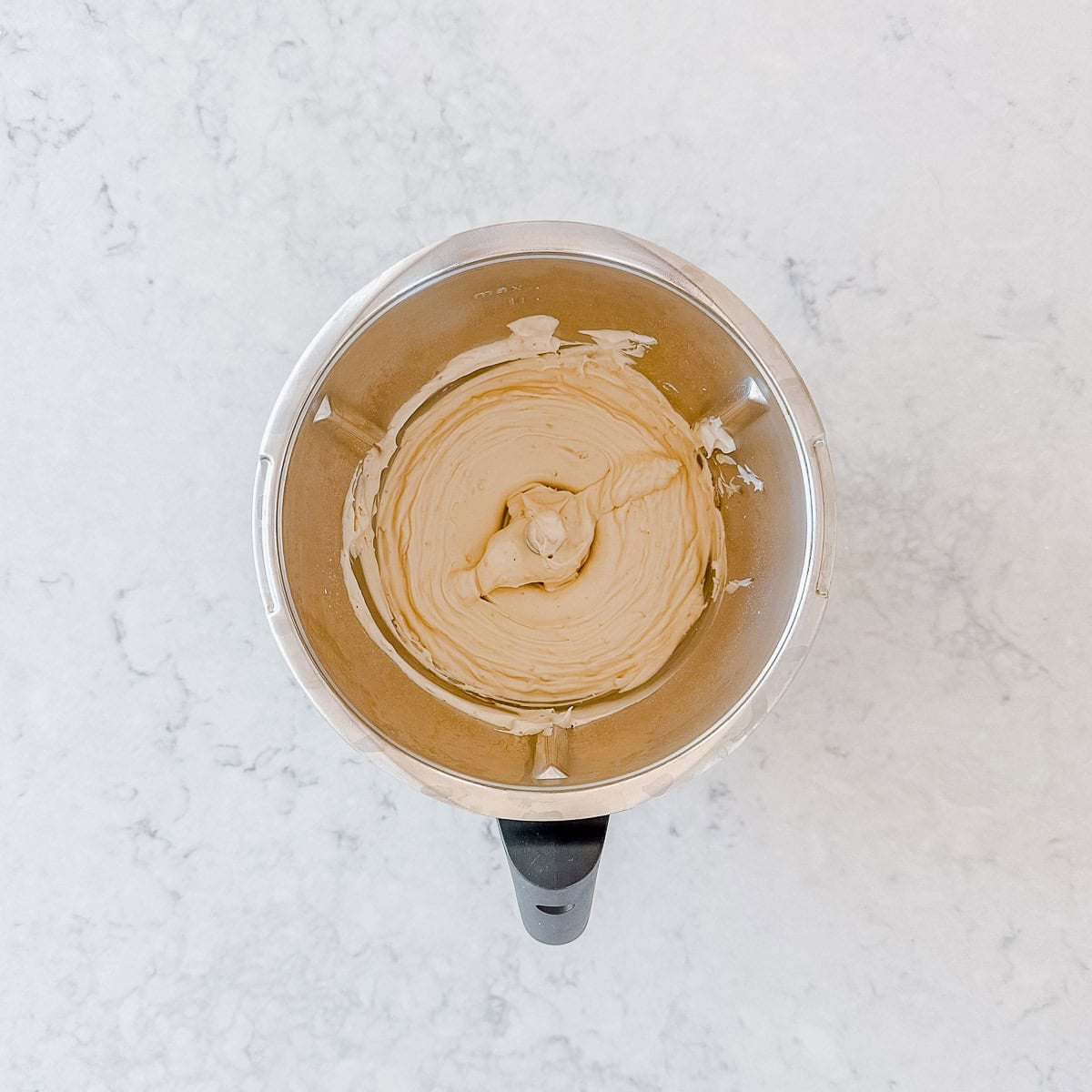 Creamy light-beige mixture being blended in a metal food processor.