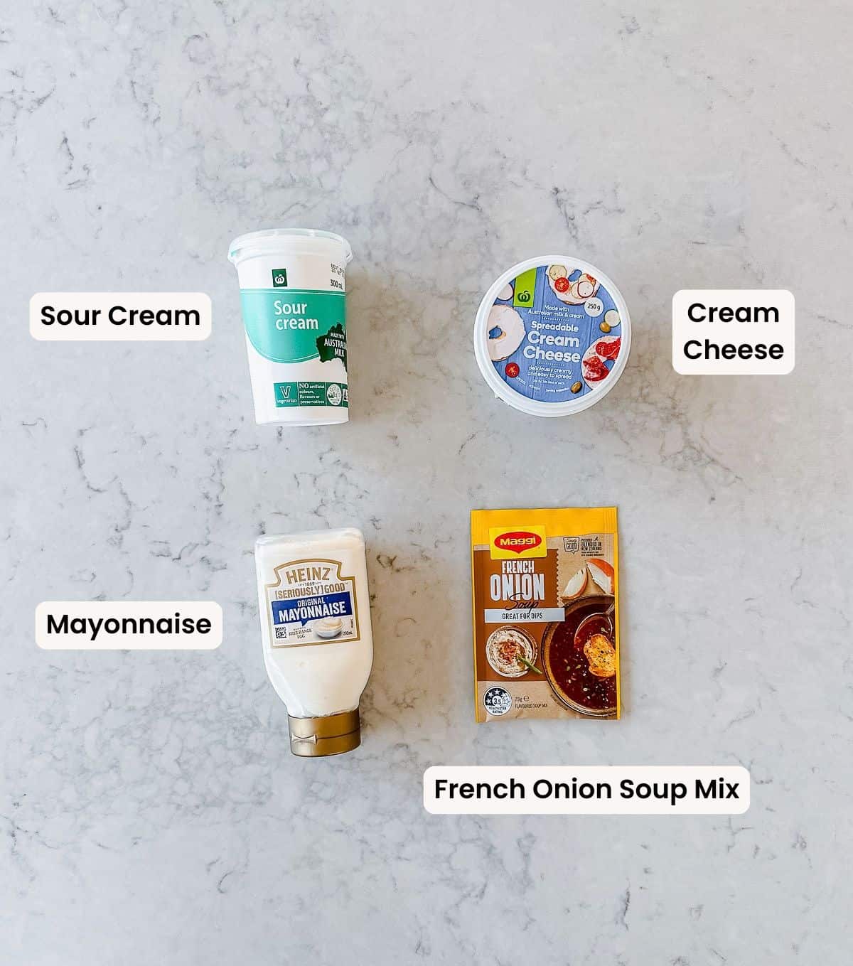A tub of soured cream, a tub of spreadable cream cheese, a bottle of Heinz mayonnaise, and a packet of Maggi French onion soup mix arranged on a marble worktop, each with a text label beside it.