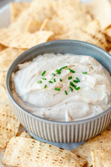 A small bowl of creamy dip topped with chopped chives, surrounded by toasted pitta chips on a platter.