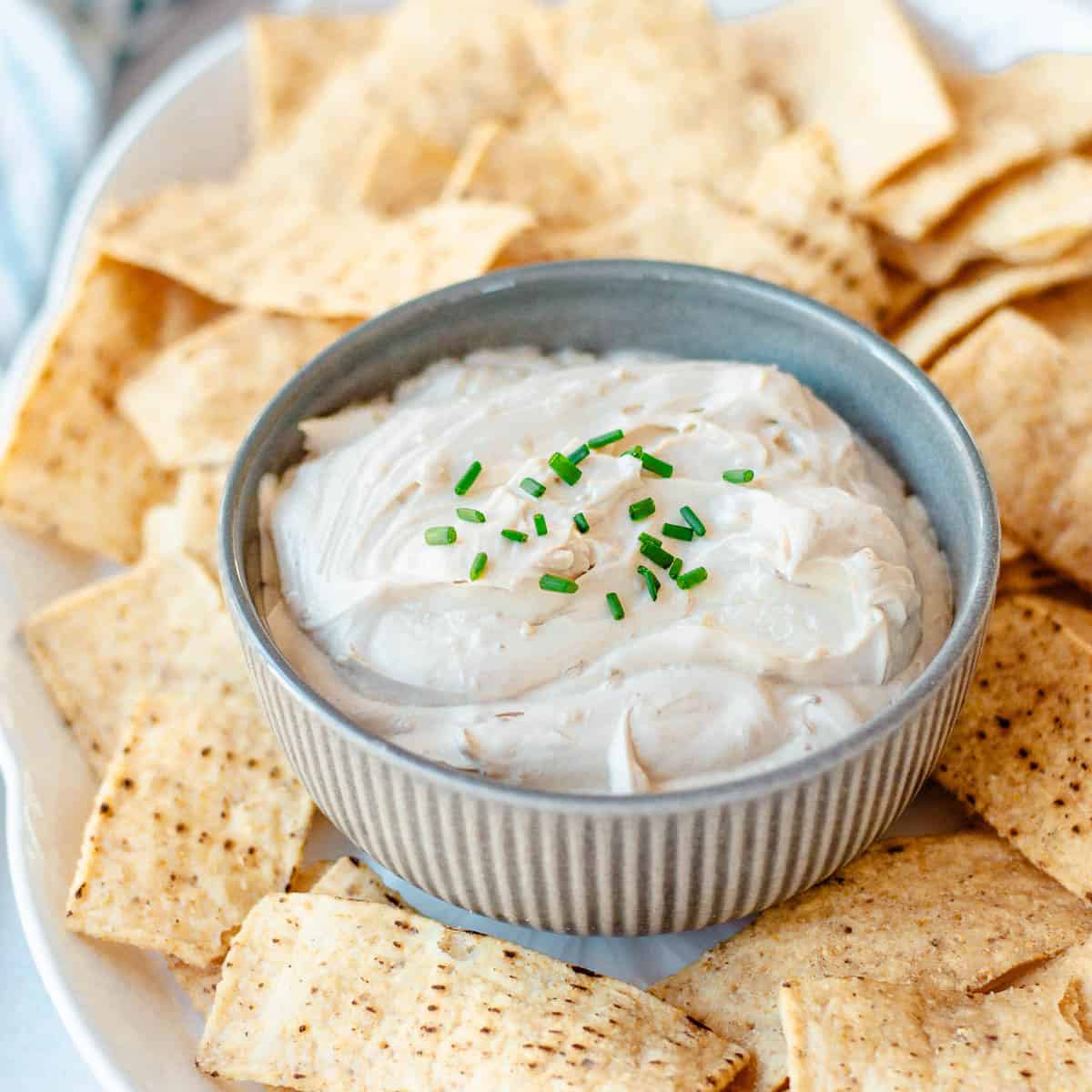 A small bowl of creamy dip topped with chopped chives, surrounded by toasted pitta chips on a platter.